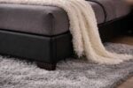 Close-up of black upholstered bed base showing smooth leather finish, sturdy wooden legs, and plush area rug underneath