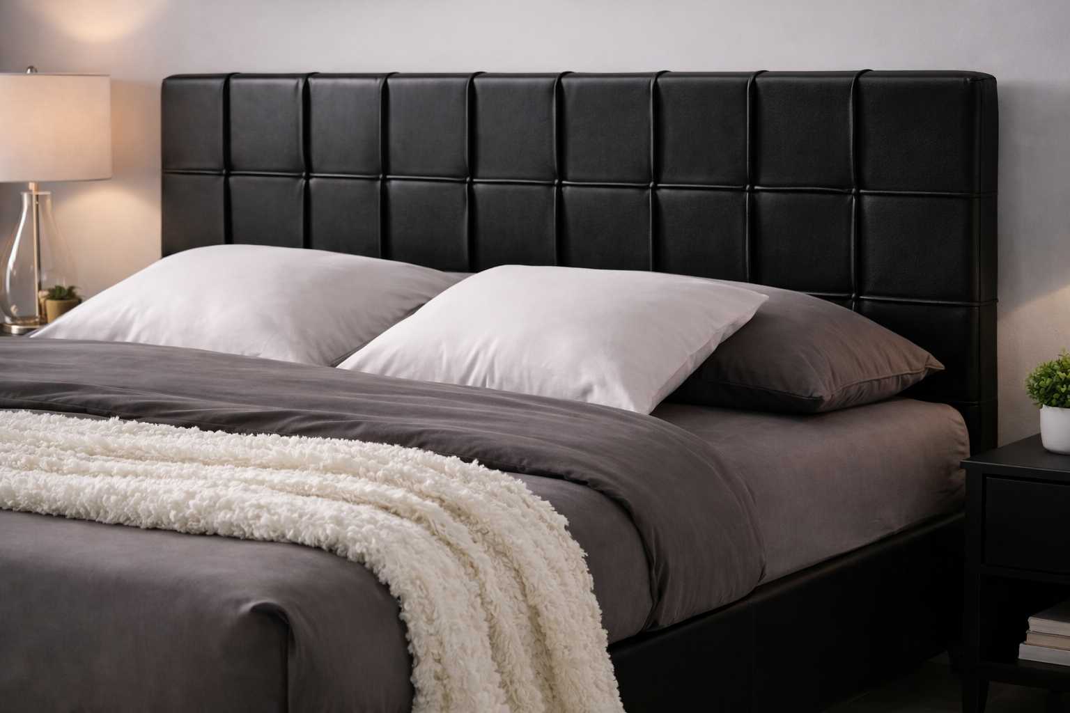 Detail view of black upholstered bed showing grey bed linen, white pillows, and soft textured throw blanket