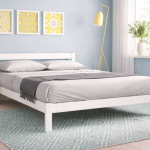 White wooden Falk bed styled in a bright modern bedroom with grey bedding, patterned rug, and soft yellow decor accents