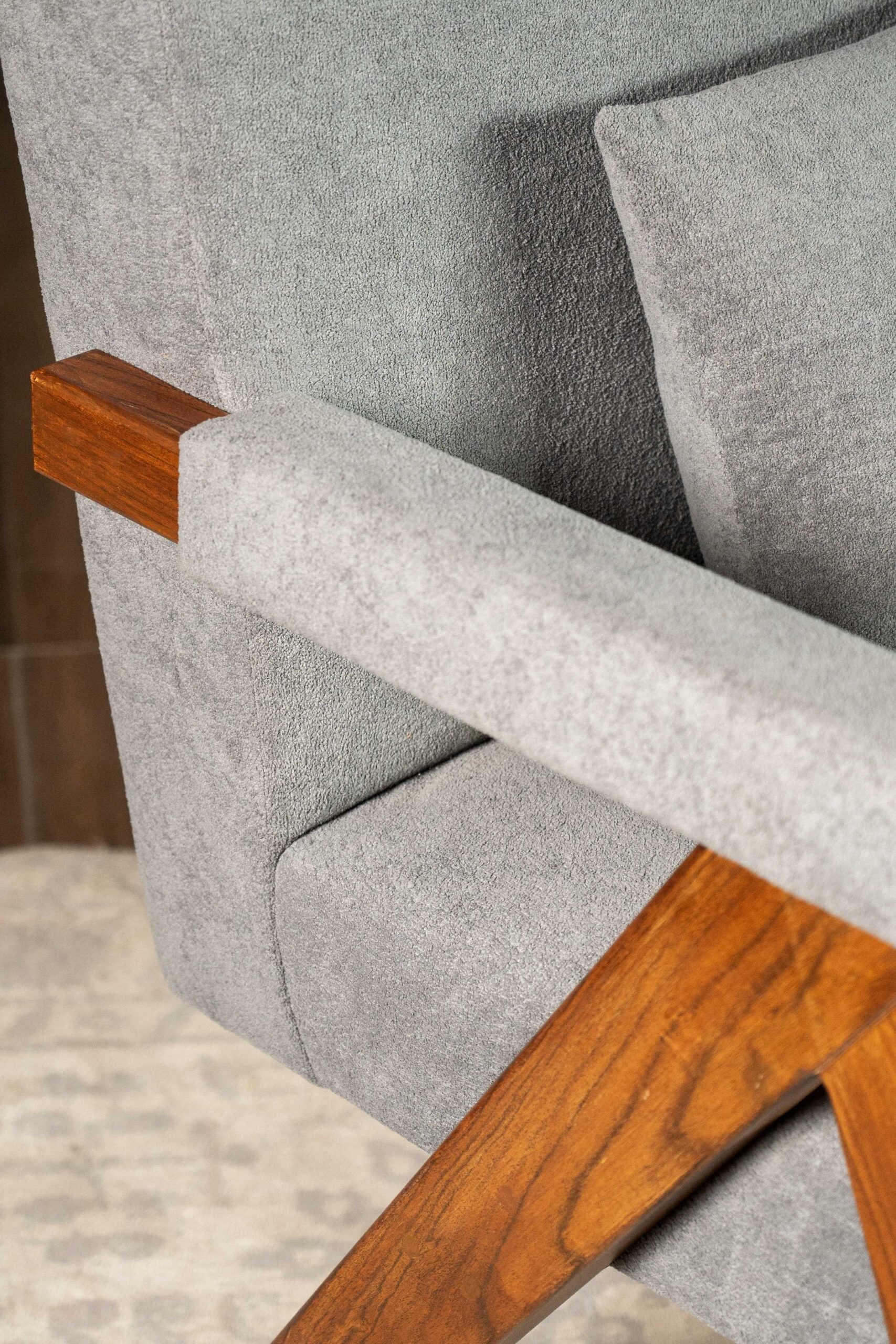 highcompress_DSC_4977 Modern upholstered armchair with soft grey fabric, featuring solid wooden armrests and angled legs, showcasing a minimalist contemporary design.