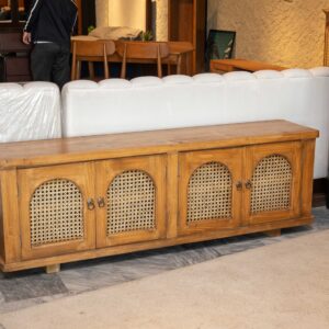 Dovelle wooden chest of drawers with cane panel doors in warm honey finish and arched design used as storage cabinet in living room interior