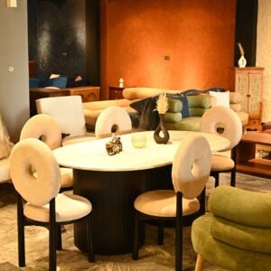Oval dining table with black fluted pedestal base and cream bouclé chairs with circular cutout backrests by Renome