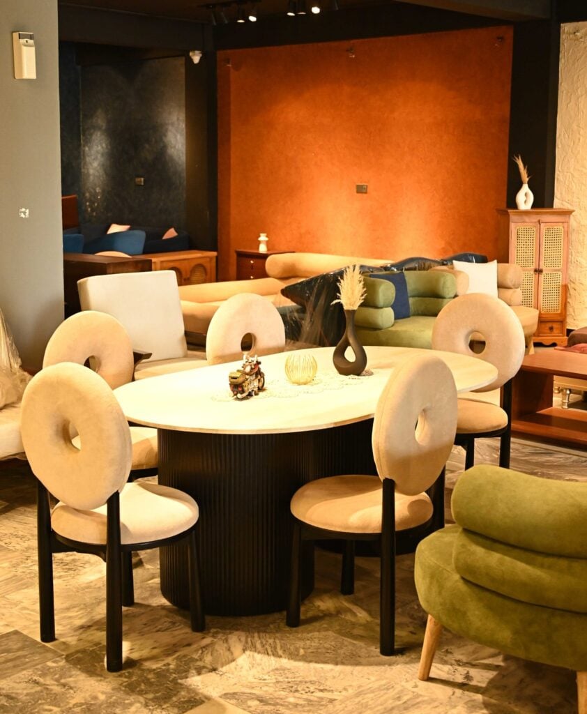 Oval dining table with black fluted pedestal base and cream bouclé chairs with circular cutout backrests by Renome